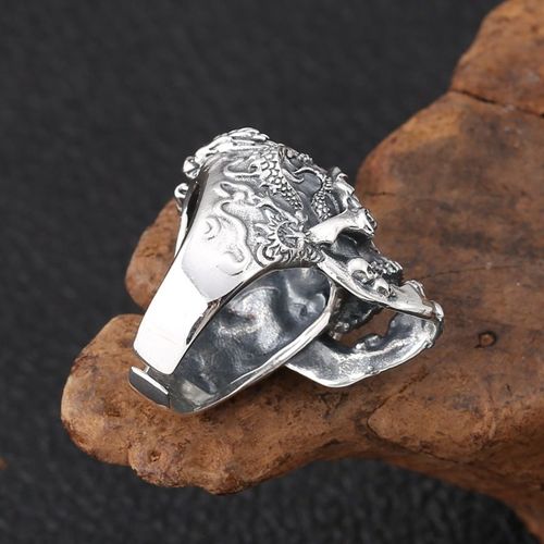 O anel poderoso retrô de estilo antigo com tema sombrio de Taibin.  O crânio principal é intricadamente esculpido.  Vários crânios pequenos estão empilhados no topo.  O ringue apresenta uma textura de padrão de dragão em loop com um estilo punk rock.  A abertura pode ser ajustada.  Este é um anel exagerado masculino para o dedo indicador.  É um anel personalizado de acessórios de moda de rua no estilo heavy metal.